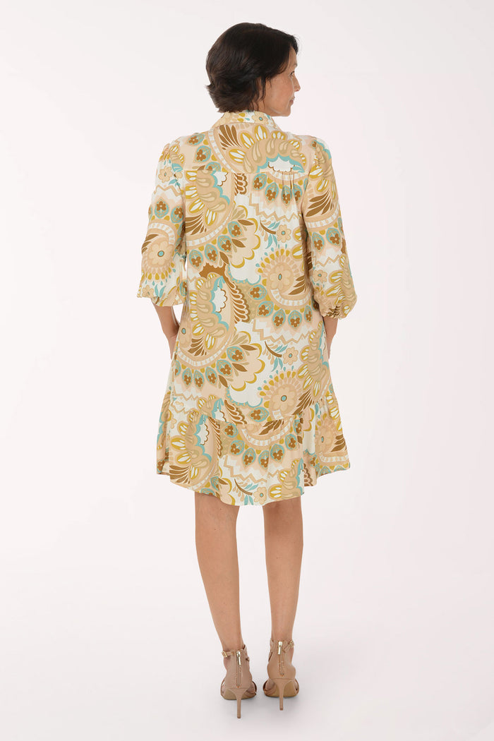 A woman modeling a short-sleeve button-up dress with a beige, gold, and light blue paisley pattern, paired with beige heeled sandals, against a plain white studio background.