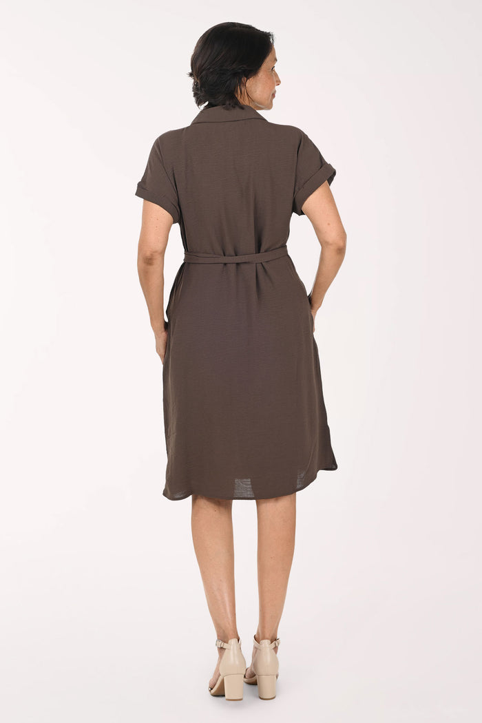A woman modeling a brown short-sleeve shirt dress with a tie waist, standing against a plain white studio background.