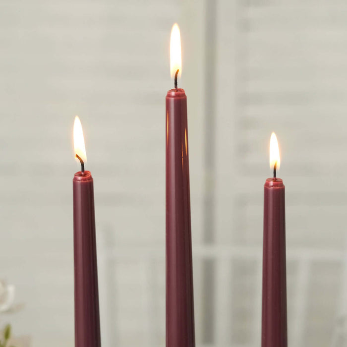 Set of three burgundy tapered candles with flames glowing on top.