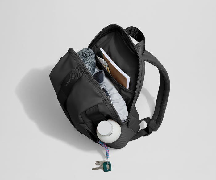 Daypack packed with a light jacket, sunglasses, notebook, map, and other travel gear. Water bottle featured in the exterior water bottle pocket.