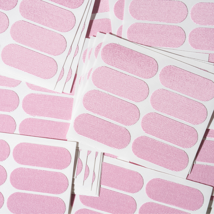 Sheets of pink adhesive strips laid out flat, showcasing multiple rounded rectangular patches for skin application, featuring Face Tape | Dreambox Beauty.