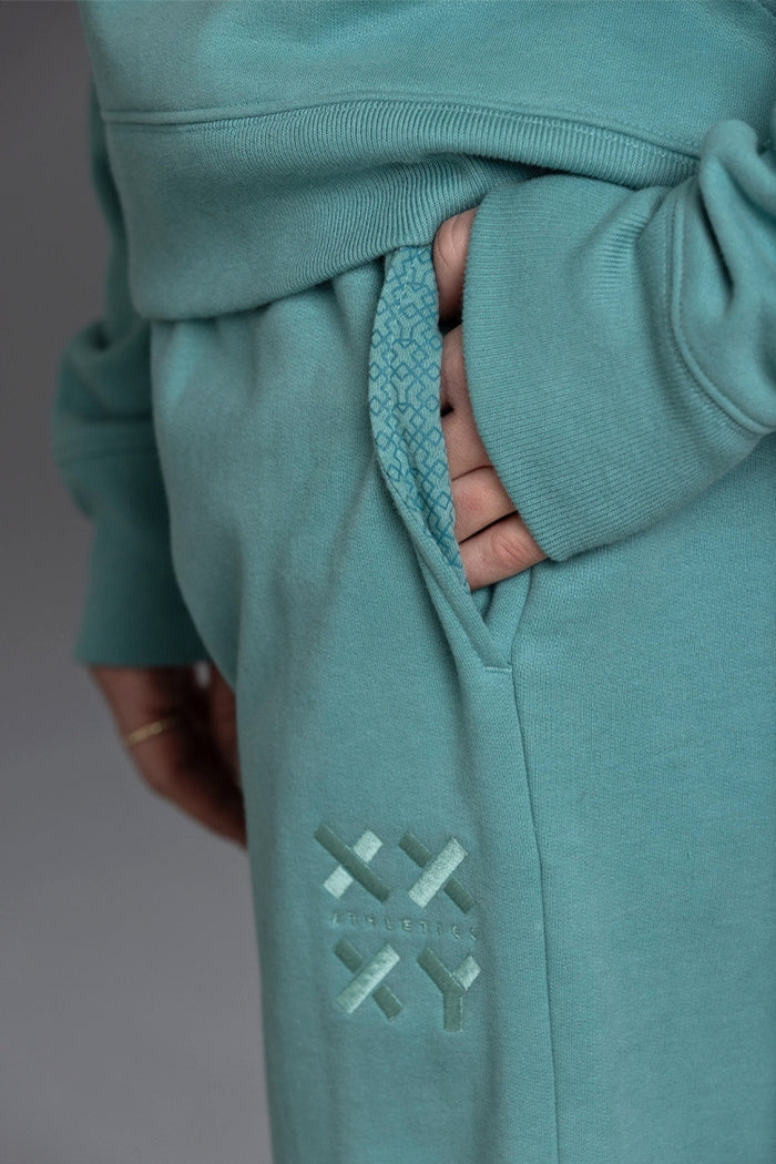 Teal tracksuit with a brand logo on the leg against a neutral background || Underseas