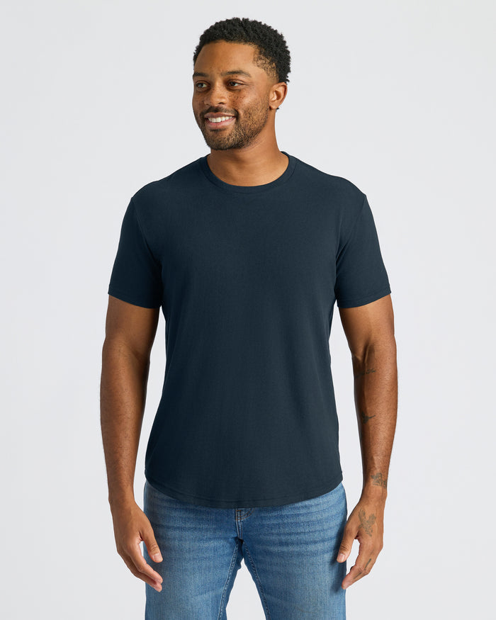 Man wearing a navy blue t-shirt and jeans on a light gray background