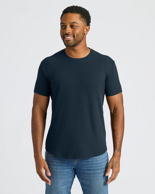 Man wearing a navy blue t-shirt and jeans on a light gray background