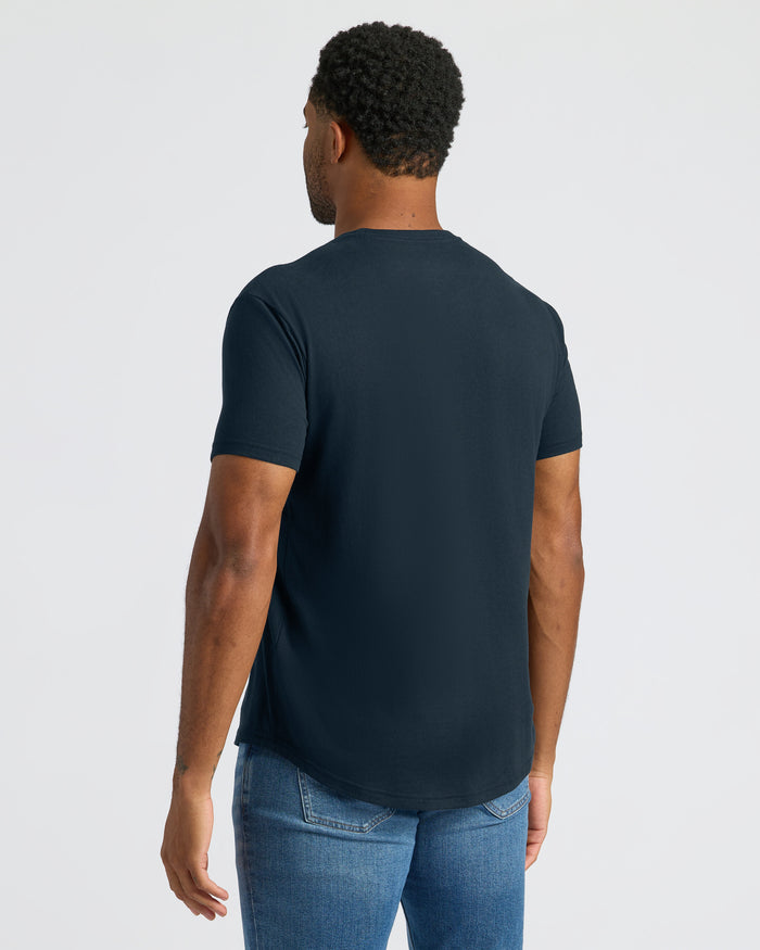 Man wearing a navy blue t-shirt and jeans on a light gray background