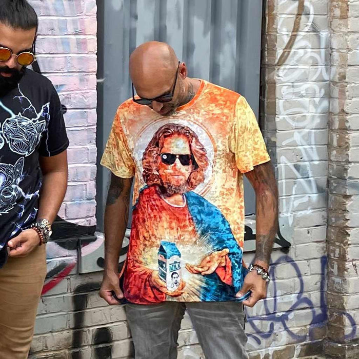 Saint The Dude T-Shirt - The specific juxtaposition of amber-tinted aviator sunglasses (#C65D21) and a casual bathrobe (#3B6B85) framed within a traditional gold-leaf religious halo (#F2AE60).