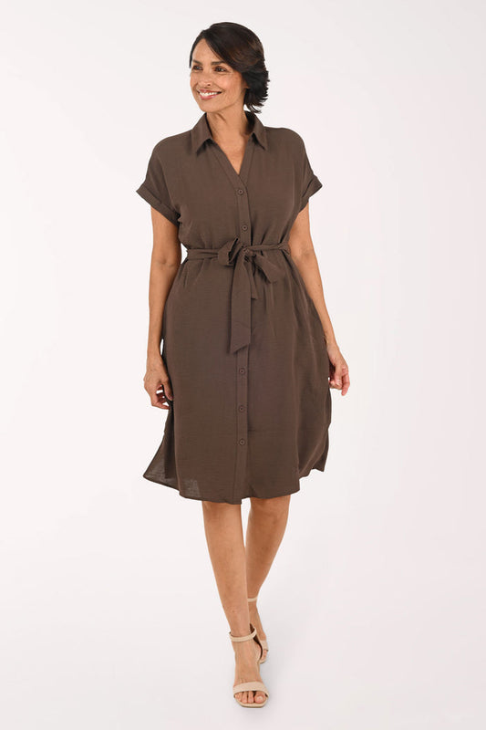 A woman modeling a brown short-sleeve shirt dress with a tie waist, standing against a plain white studio background.